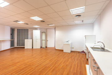 Old empty room with white kitchen furniture and sink that used to serve as office canteen for employees. A spacious and bright room, equipped as corporate dining room, needs new and fresh renovation.