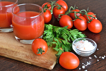 tomato juice in drinking glass on cutting board with cherry tomatoes, parsley and salt