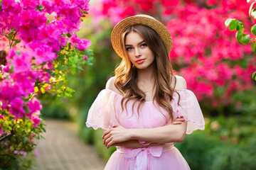 Beautiful  girl in pink  vintage dress and straw hat standing in garden near colorful flowers. Art work of romantic woman .Pretty tenderness model looking at camera.