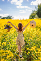 girl with flowers and a hat in a field of rapeseed. Yellow flower field. View from the back