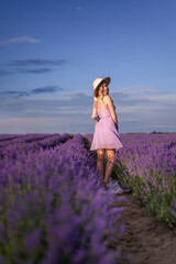 beautiful young woman in a hat and a short lilac dress is spinning in a field of lavender