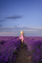 girl in a hat and a lilac dress runs into a field of lavender. View from the back