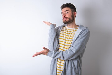 caucasian man wearing casual sportswear over white wall pointing aside with both hands showing...
