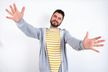 Naklejka premium caucasian man wearing casual sportswear over white wall looking at the camera smiling with open arms for hug. Cheerful expression embracing happiness.