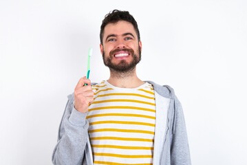 caucasian man wearing casual sportswear over white wall holding a toothbrush and smiling. Dental healthcare concept.