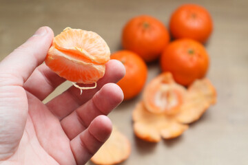 Man with fresh tangerine at table indoors. View from above. Close-up of yummy healthy mandarin fruit. Macro shot of man holding bright orange tangerine on camera.