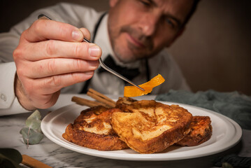 A waiter chef places orange zest on a set of gourmet torrijas with tongs. A typical Spanish sweet made with bread, milk, eggs, sugar, and cinnamon that is eaten during Carnival and Easter - obrazy, fototapety, plakaty