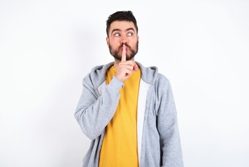 caucasian man wearing casual sportswear over white wall silence gesture keeps index finger to lips makes hush sign. Asks not to share secret