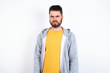 Fototapeta premium Offended dissatisfied caucasian man wearing casual sportswear over white wall with moody displeased expression at camera being disappointed by something