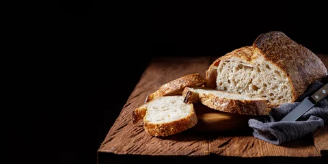 Gardinen Rustic sourdough bread with cut slices on a wooden table. Panorama, black background with free space for text. © Sergey