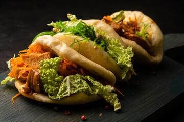 Asian steamed bao buns filled with chicken and vegetables on a dark board.