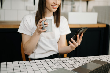 Fototapeta premium woman using laptop and typing on laptop and holding coffee cup in cafe, home office in morning light.