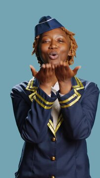 Vertical video: Female aircrew member sending air kisses on camera, acting flirty and cute in studio. Young stewaress dressed in uniform showing romantic sweet gesture, doing kissy face. Aviation job.
