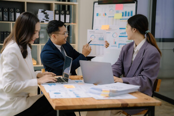 Fototapeta premium Business documents on office table with tablet and laptop computer and chart and asian team colleagues discussing data in office.