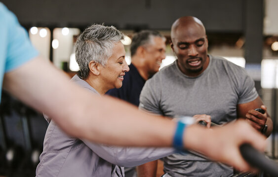 Senior group, exercise bike and personal trainer for fitness, time and retirement wellness by blurred background. Elderly woman, bicycle training or diversity with black man, stopwatch and motivation