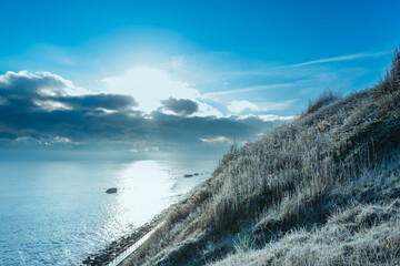 Cold, early morning view of a sloping cliff covered with frost. A distant snow storm is seen on the horizon, out to sea.
