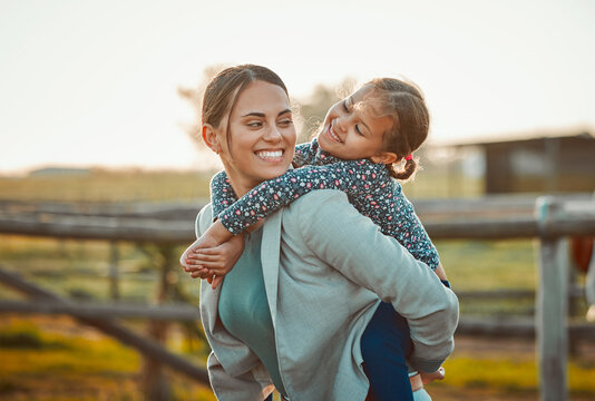 Mother, young girl and hug of a kid piggy back fun and parent care outdoor in equestrian field. Mom smile, child happiness and family in nature with blurred background in summer on holiday in a park