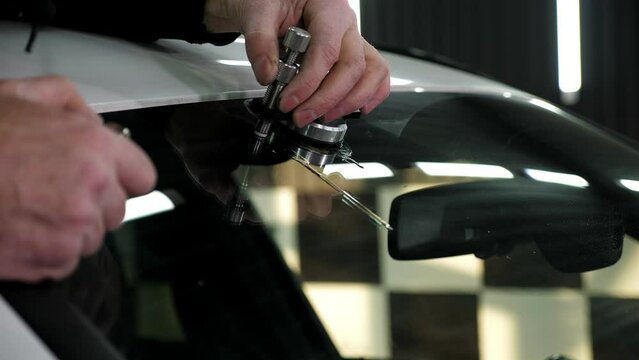 Specialist repairs dangerous crack in windshield on location without replacement glass for free. Mechanic using repairing equipment to fix damaged windshield.