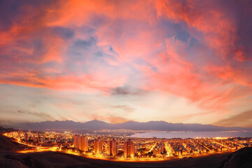 Sunrise panoramic view of Eilat. Israel.  Glowing town lights at night. Red Sea. Lights of Aqaba, Jordan city on the opposite side of the bay (gulf). Jordan mountains in the in the foggy distance
