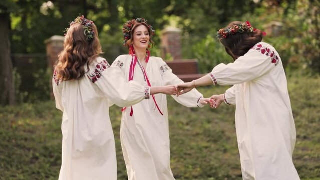 Three women in round dance roundelay. Girls wear Ancient ethno Ukrainian embroidered shirt dress and a wreath of flowers. Medium shot