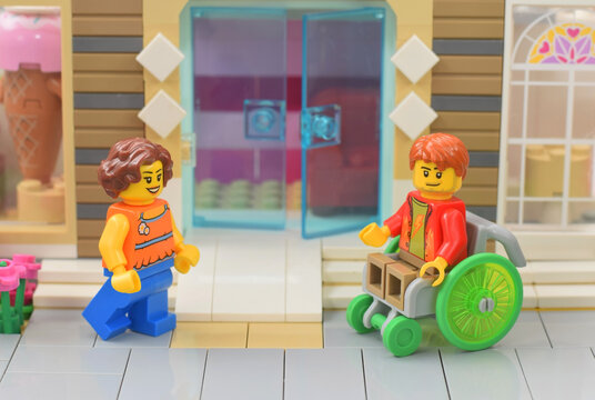 Lego minifigure of girl is in front of pandas and man in chair. Editorial illustrative image of popular plastic bricks toy. Studio shot.