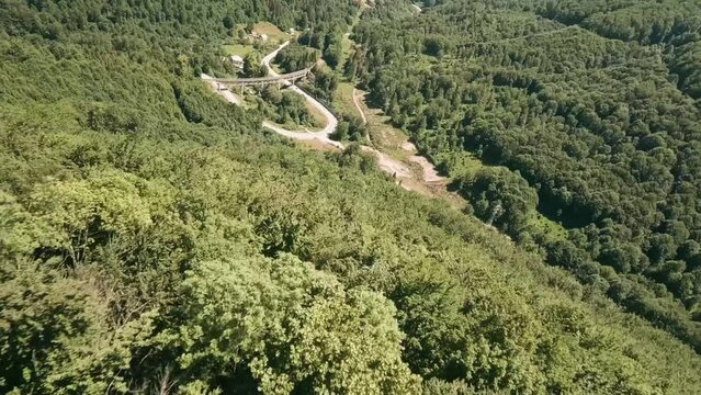 Dynamic flying with FPV racing drone close above the treetops. Descending fast towards an old  old railway bridge and a winding road. LuPa Creative.