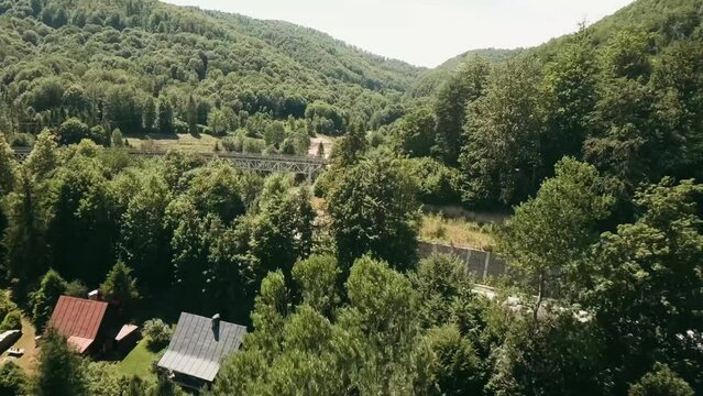 Dynamic aerial view with FPV racing drone flying above cottages and under an old railway bridge alongside an empty winding road. LuPa Creative.