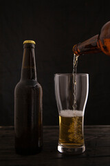 A stream of beer from the bottle pours into the beer glass, causing a lot of bubbles and foam.