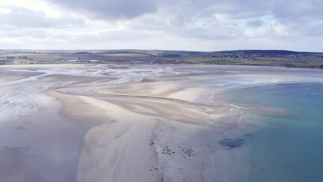 Drone shot of a river meeting the sea at Gress beach at low tide on the Outer Hebrides of Scotland.
