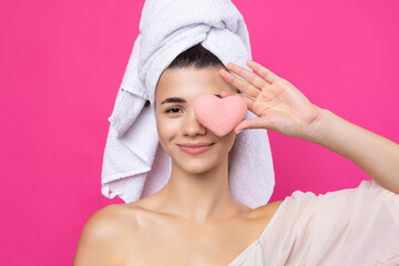 Beautiful cheerful attractive girl with a towel on her head, holds a sponge in the form of a pink heart.