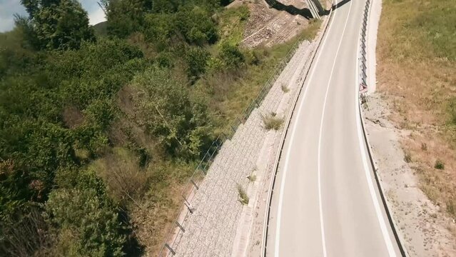 Dynamic flying with FPV racing drone along a winding road and under and above an old railway bridge passing by a red van and other cars. LuPa Creative.