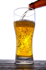 A stream of beer from the bottle pours into the beer glass, causing a lot of bubbles and foam.