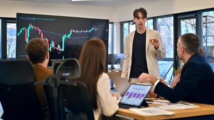 Young worker leading business meeting in an office, discussing the topic of cryptocurrencies with other workers using a big display with currency rate and physical coin. Slow motion - Powered by Adobe