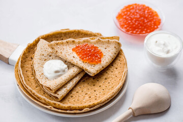 Russian traditions. Broad Maslenitsa. A stack of pancakes, sour cream and red caviar on a light background. Close-up.