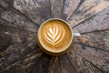 Top view of cup of aromatic cappuccino with latte art served on wooden table in cafe