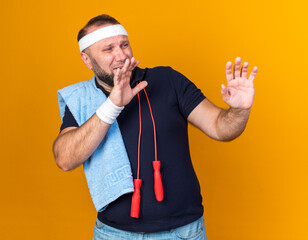scared adult slavic sporty man with jumping rope around neck wearing headband and wristbands...