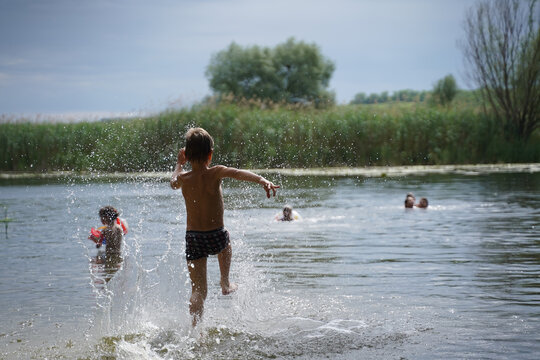 Happy boy run from the shore into the water. Summer childrens vacation on shore of lake or river. kid jump into water, swim and splash around at sunset. Active holidays. Dynamic image. Selective focus