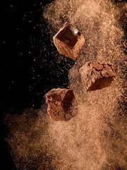 Brownie pieces in dry cocoa powder explosion on black background