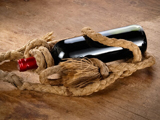 Red wine bottle, wrapped with hemp rope on wood