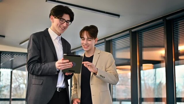 Two young workers discussing business affairs using a tablet in an office. Slow motion