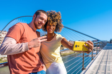 Multiracial couple through the city streets, lifestyle, selfie smiling by the river, victory gesture