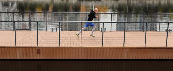 A young man in warm sportswear runs in the city embankment. Morning running workout on the bridge near the river. The concept of a healthy lifestyle, fitness, sport.