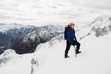 Hiker wearing a protective helmet and sunglasses looking up while on a hike up the snowy mountain - obrazy, fototapety, plakaty