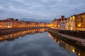 The nightscape of the river Arno and Santa Maria della Spina in Pisa, Italy. Cloud reflection in the river, night lights and mountains in the background