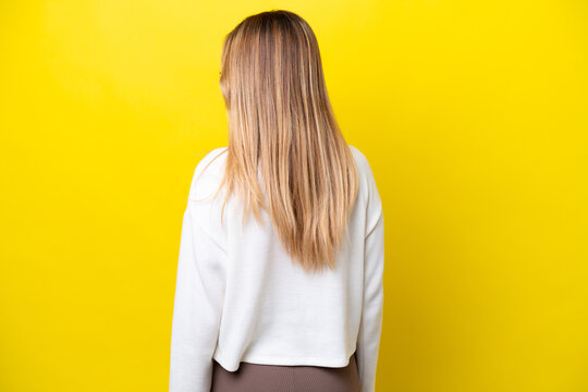 Young Uruguayan woman isolated on yellow background in back position and looking side
