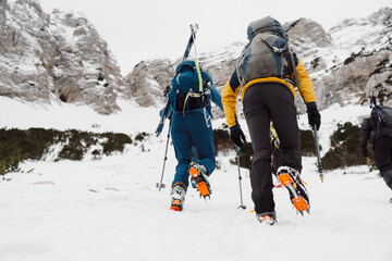 View from the back, two unrecognizable mountaineers climbing up a steep snowy mountain in the...