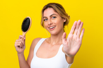 Young Uruguayan woman with hair comb isolated on yellow background saluting with hand with happy expression