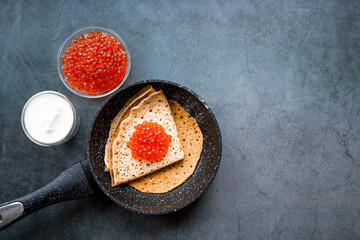 Russian traditions. Broad Maslenitsa. Pancakes in a frying pan, and red caviar on a dark background. Close-up