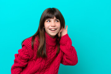 Little caucasian girl isolated on blue background listening to something by putting hand on the ear