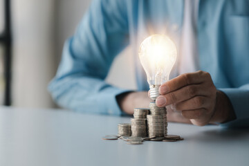 Businessman holds a glowing light bulb on top of the highest pile of coins, Placing coins in a row from low to high is comparable to saving money to grow more. Money saving ideas for investing in fund